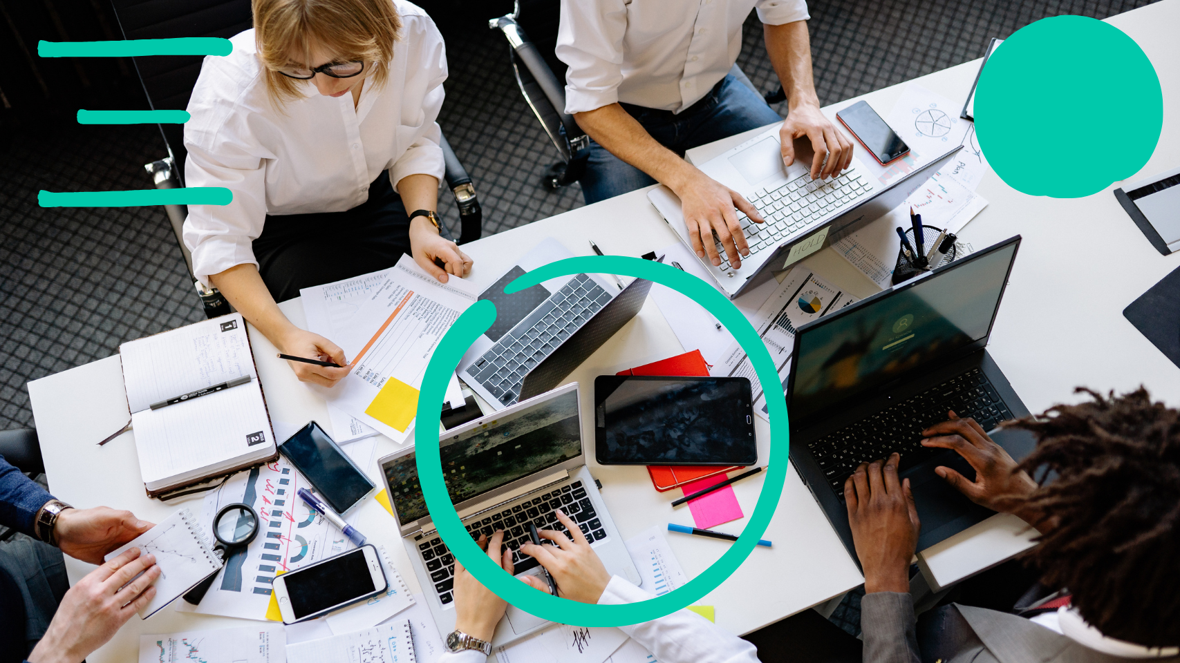 A group of people are gathered around a white table, working on laptops and reviewing documents. The scene is viewed from directly above.