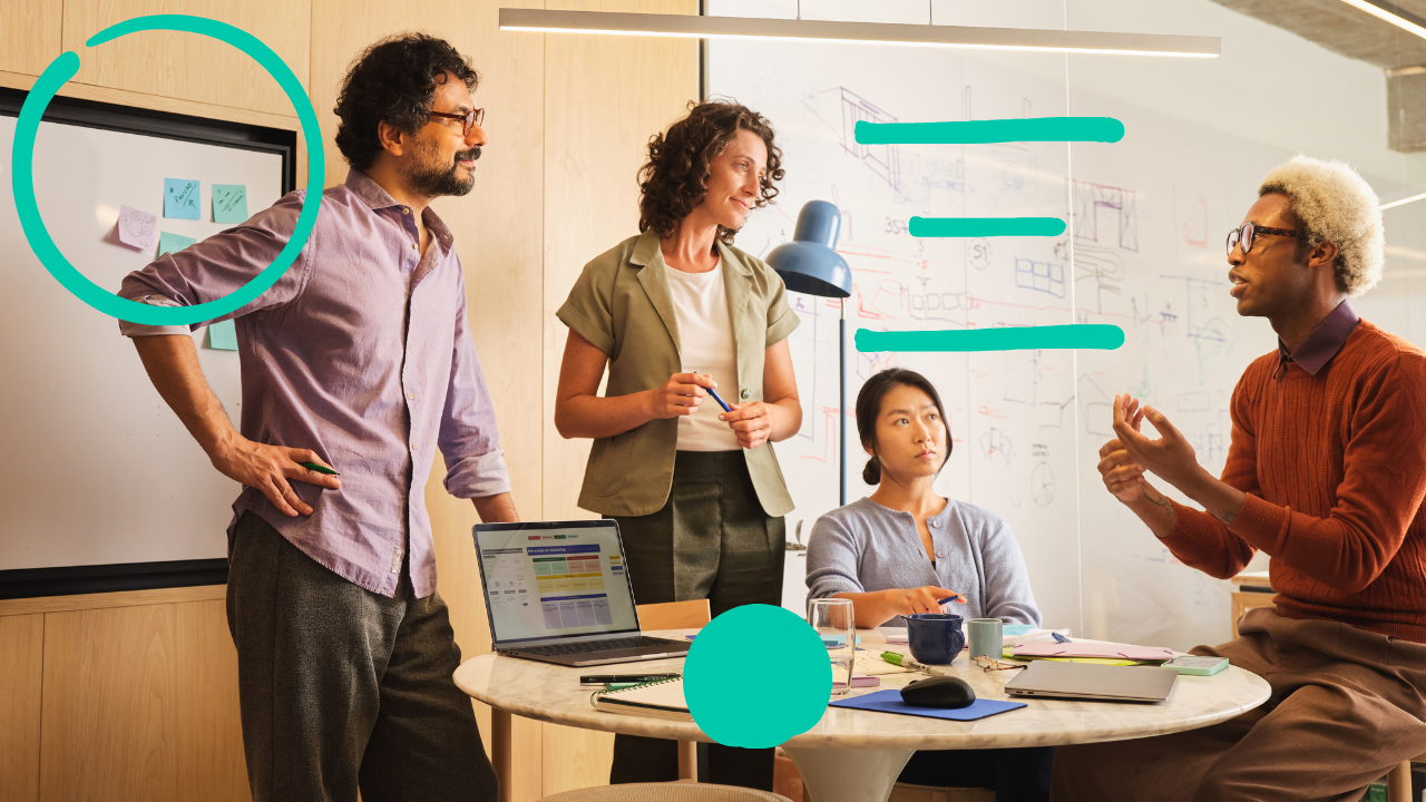 A group of people in a meeting room discussing ideas around a table with a laptop and whiteboard.